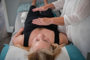 Image of a lady lying down with hands hovering above as she is treated with reiki to support her wellbeing